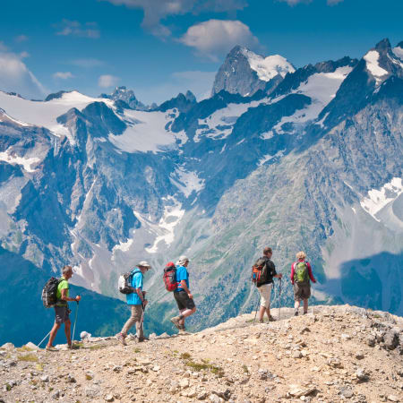 Groupe de randonneurs équipés de sacs à dos face à chaîne montagneuse enneigée avec sommets de 3000m et glacier