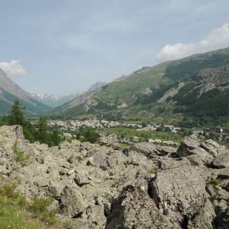 Randonneurs sur sentier rocheux en montagne avec vue sur vallée alpine et village en contrebas à Serre Chevalier
