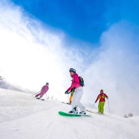 Trois skieurs en tenue colorée descendant une piste enneigée à Chamonix sous un ciel bleu dégagé