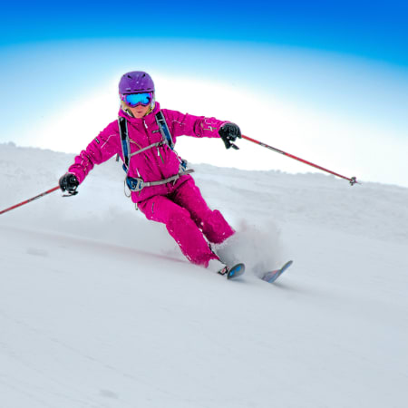 Skieur expert en tenue rose vif dévale une pente hors-piste enneigée avec bâtons de ski et équipement de sécurité