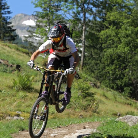 Cycliste en VTT descendant un sentier alpin verdoyant avec casque et équipement de protection près du Mont-Blanc