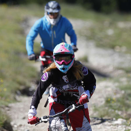 Jeune rider en VTT de descente avec casque et lunettes de protection sur un sentier de montagne à Serre Chevalier
