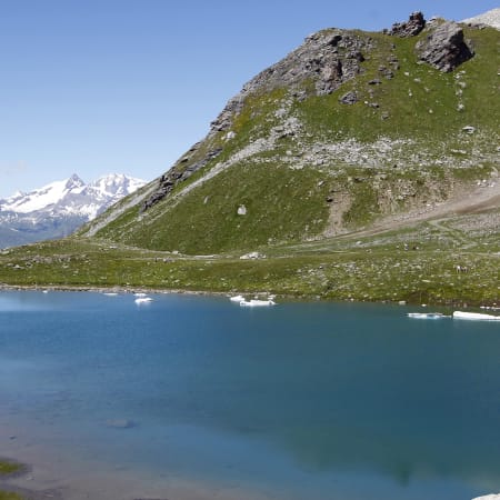 Lac alpin turquoise en Haute Tarentaise entouré de pentes vertes et de pics enneigés aux Arcs