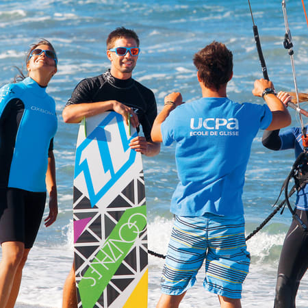 Moniteurs et élèves en cours de kitesurf à la plage avec planches et équipement, mer turquoise en arrière-plan