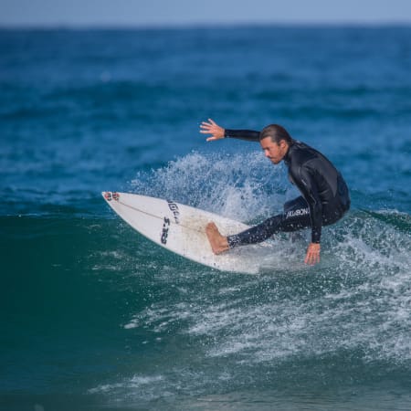 Surfeur en combinaison noire chevauchant une vague avec sa planche blanche sur l'océan