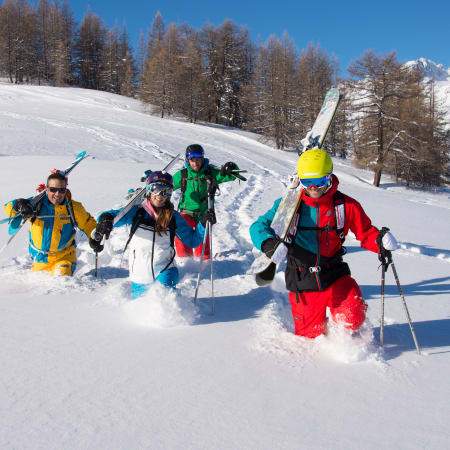 Groupe de skieurs hors-piste en poudreuse fraîche à Serre Chevalier avec mélèzes et pics enneigés en arrière-plan