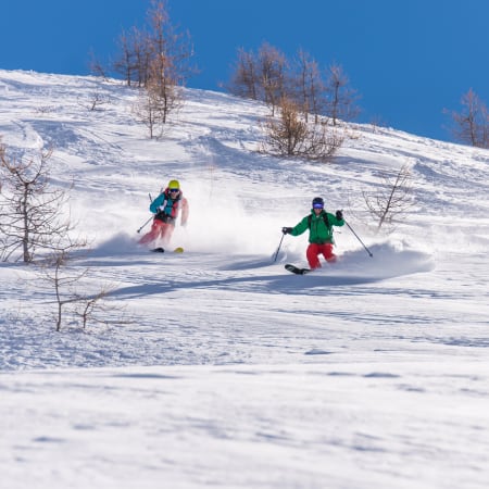 Deux skieurs en action dévallant une pente enneigée hors-piste à Chamonix sous un ciel bleu dégagé