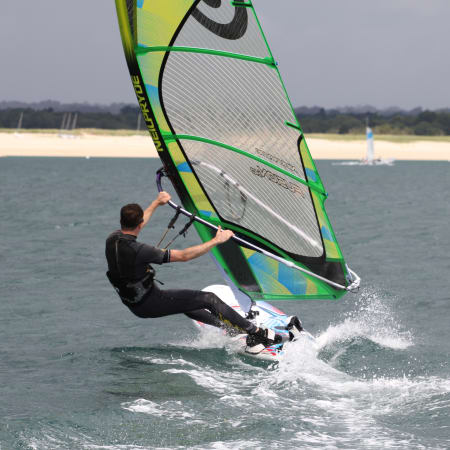 Pratiquant de windsurf en action sur la lagune bretonne avec voile verte et jaune, dunes en arrière-plan