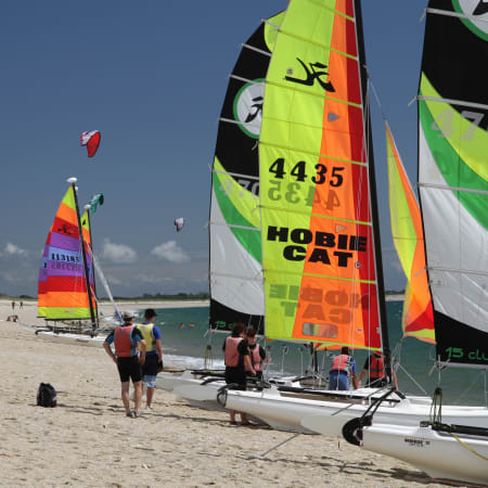 Jeunes participants préparant des catamarans à voile colorés sur la plage de Bénodet pour un stage nautique