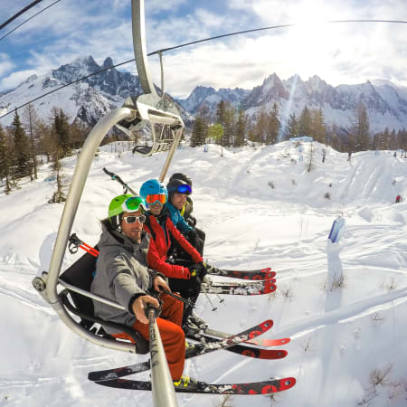 Trois jeunes skieurs en remontée mécanique dans les Alpes avec pentes enneigées et forêt alpine en arrière-plan