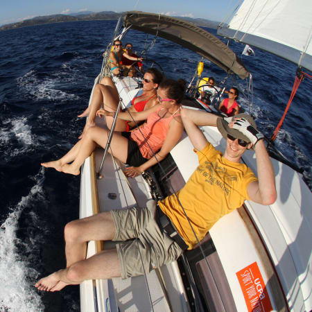 Voilier en navigation avec passagers profitant d'une croisière en Corse sous le soleil, voiles blanches déployées sur mer méditerranéenne bleue