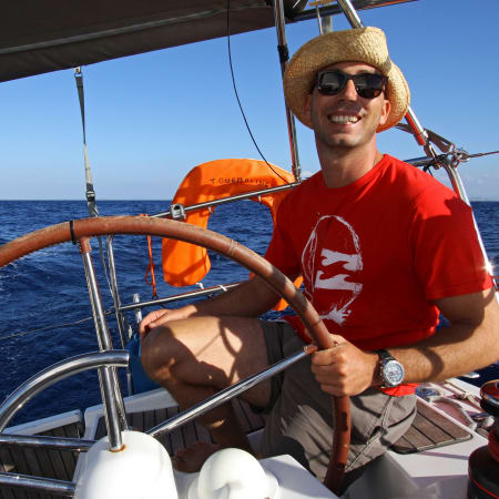 Stagiaire souriant tenant la barre du voilier en Méditerranée lors d'une croisière en Corse