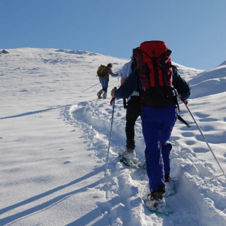 Randonneurs en raquettes progressant dans la neige fraîche en montagne enneigée sous ciel bleu