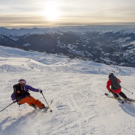 Skieurs en descente sur pente enneigée des Alpes avec vue panoramique sur la vallée et montagnes lointaines