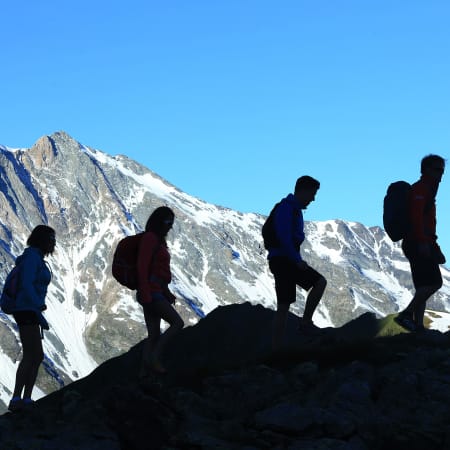 Groupe de randonneurs en trek alpestre dans la vallée de Valgrisenche avec montagnes enneigées en arrière-plan