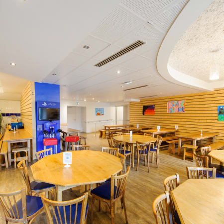 Espace de loisirs moderne à Argentière avec tables rondes en bois, chaises bleues et murs jaunes accueillant familles en vacances