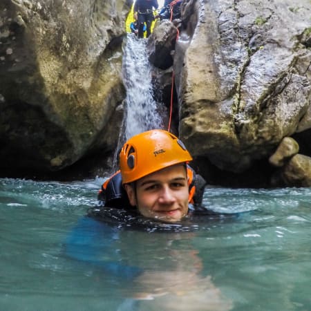 Participant en casque orange pratiquant le canyoning dans une gorge avec cascade et eaux turquoise