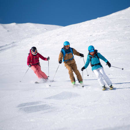 Trois skieurs en formation encadrée descendant une piste enneigée à Serre Chevalier sous ciel bleu
