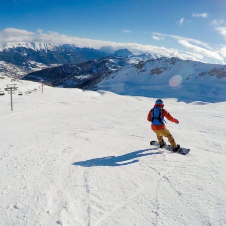 Skieur en veste rouge dévale les pistes enneigées de Serre Chevalier avec vue panoramique sur les Alpes et remontées mécaniques
