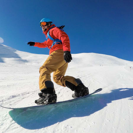 Skieur en veste rouge descendant une piste enneigée des Arcs sous un ciel bleu dégagé