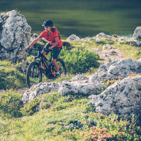 Cycliste en maillot rouge pratiquant le VTT sur sentier montagneux des Pyrénées avec rochers et végétation alpine
