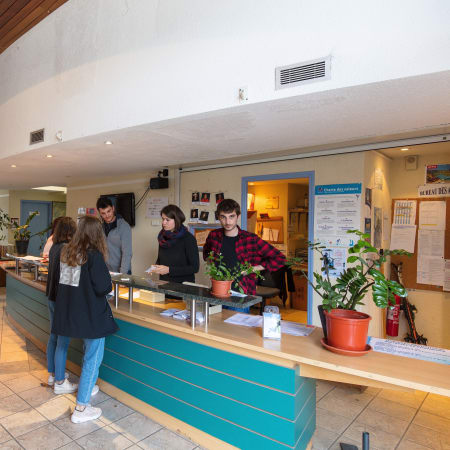 Accueil touristique de Saint-Lary-Soulan avec réceptionniste et visiteurs au comptoir, plantes décoratives et informations sur la destination