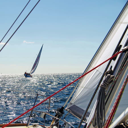 Voilier en navigation en Bretagne avec vue depuis le pont montrant les cordages, les voiles et un autre bateau à l'horizon au large de Groix