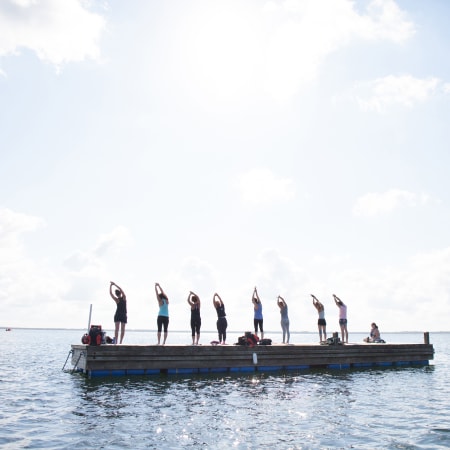Groupe de participants en cours de yoga debout sur une plateforme flottante en mer à Bombannes