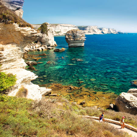 Falaises blanches de Corse surplombant une mer turquoise avec randonneurs sur le sentier côtier et rochers sculptés
