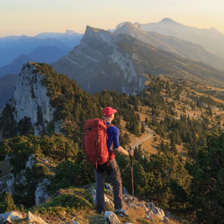Randonneur avec sac à dos rouge admirant la vue sur le Massif du Vercors et le Mont-Aiguille au coucher de soleil