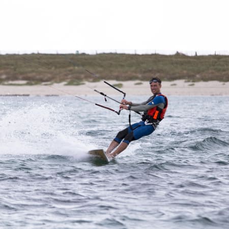 Kitesurfeur en combinaison bleue pratiquant le kitesurf en lagune bretonne avec dunes en arrière-plan