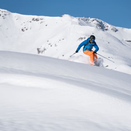 Skieur en veste bleue descendant une pente vierge enneigée en ski freerando en montagne