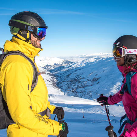 Deux skieurs en tenue colorée face aux pistes enneigées de Chamonix et la vallée du Mont-Blanc sous ciel bleu