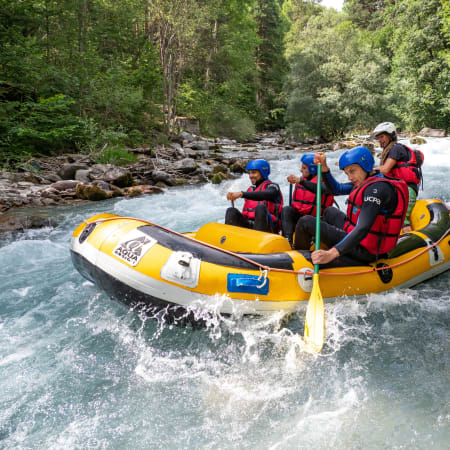 Groupe de rafting en eaux vives sur un radeau jaune dans une rivière de montagne entourée de forêt dense