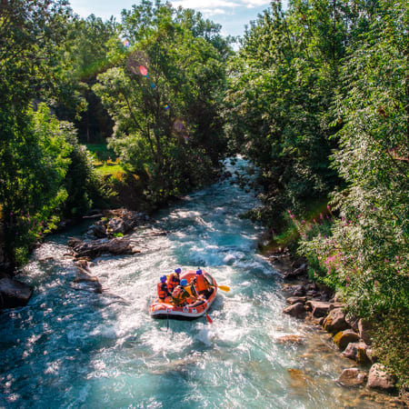 Groupe en rafting sur eaux vives turquoise encadrées de végétation luxuriante lors d'une descente multisports