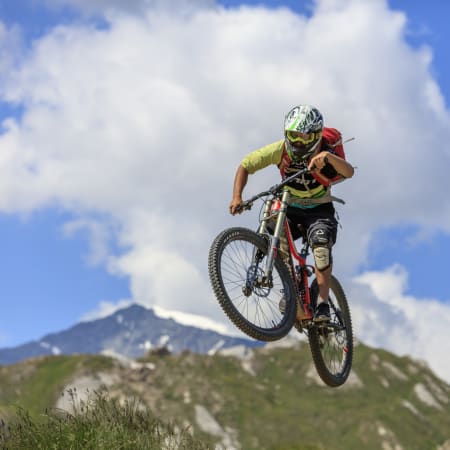 Coureur en VTT descente sautant en l'air sur un terrain montagneux avec paysage alpin en arrière-plan