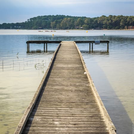 Ponton en bois sur le lac de Carcans avec base nautique et voiliers en arrière-plan pour stage de planche à voile