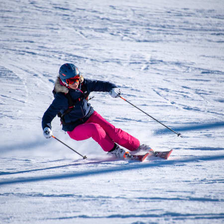 Skieur en action aux Deux-Alpes avec casque bleu et tenue rose descendant une piste enneigée