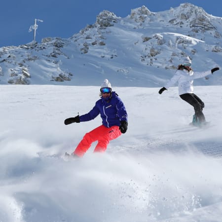 Moniteur et élève en cours de snowboard sur une piste enneigée avec montagne rocheuse en arrière-plan