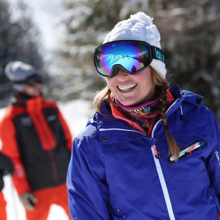 Jeune skieuse souriante en veste bleue et bonnet blanc avec masque de ski miroir dans la Vallée de Chamonix