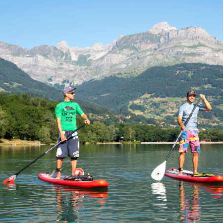 Deux pratiquants en stand up paddle sur un lac de montagne avec paysage alpin enneigé en arrière-plan