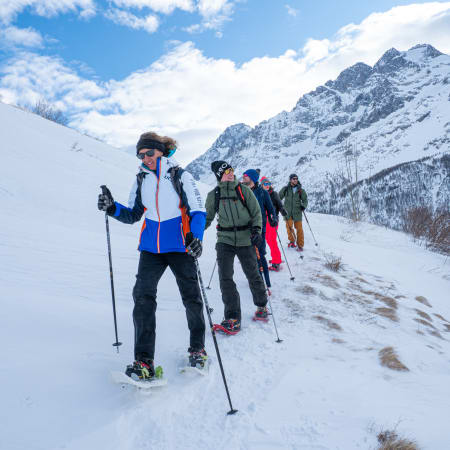 Groupe de randonneurs en raquettes altitude traversant une vallée enneigée des Alpes italiennes avec montagnes majestueuses