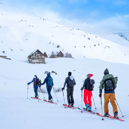 Groupe de randonneurs en ski de montagne équipés de sacs à dos montant une pente enneigée à Chamonix avec chalets alpins