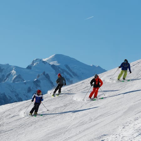 Groupe de jeunes skieurs descendant une piste aux Deux-Alpes avec sommets enneigés en arrière-plan