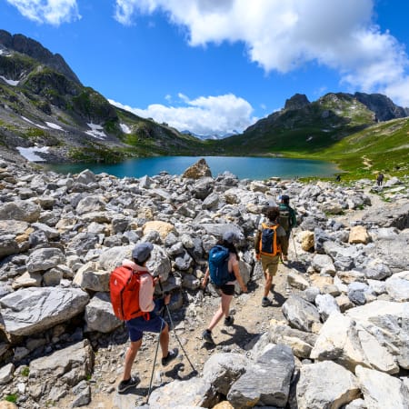 Randonneurs en groupe devant un lac alpin turquoise entouré de montagnes rocheuses et de prairies vertes à Serre-Chevalier