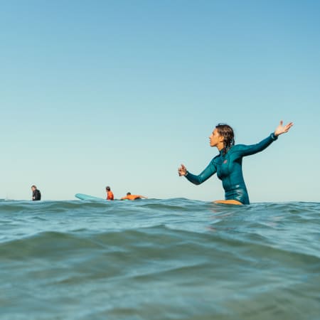 Surfeur en combinaison bleue dans l'océan à la Pointe de la Torche avec groupe de stagiaires et planches de surf