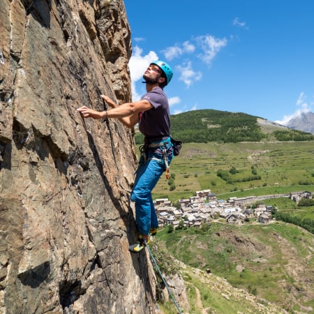 Grimpeur en escalade sur une falaise rocheuse avec vue sur la vallée de Serre Chevalier et les montagnes alpines
