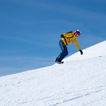 Snowboardeur en veste jaune descendant une piste enneigée sous un ciel bleu dégagé à Serre Chevalier