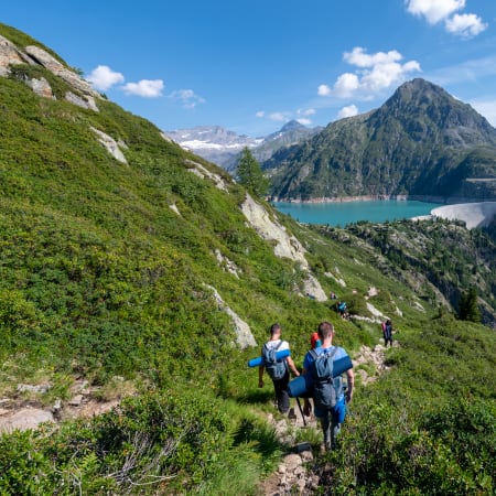 Randonneurs en sentier montagnard avec vue sur lac alpin et sommets enneigés du Mont-Blanc