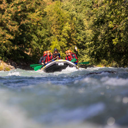 Groupe de rafters en gilets de sauvetage rouge naviguant les rapides d'une rivière de montagne entourée de forêt verdoyante